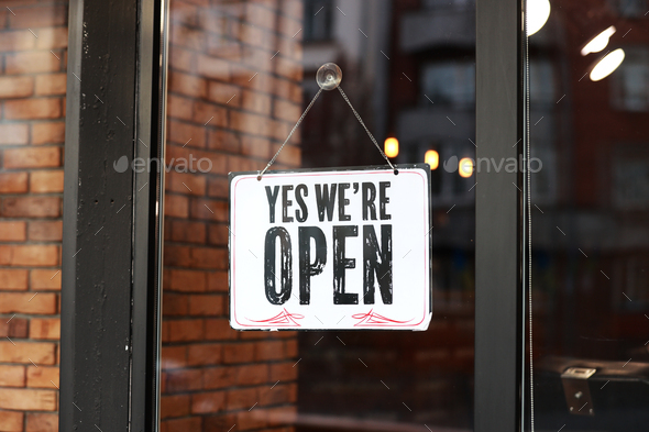 Inscription Yes we're open metal plate with black and white sign on glass door store, cafe,