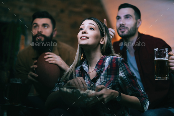 Young woman eating popcorn while watching sports match on TV with friends.