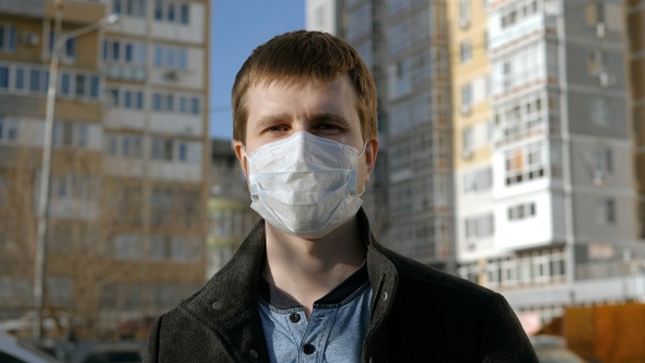 Man in a surgical mask standing outdoors and looking to camera. alt