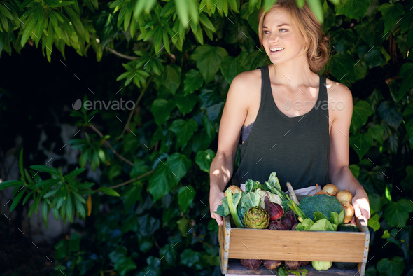 Eat better, feel better. A young woman holding a crate of vegetables outdoors.