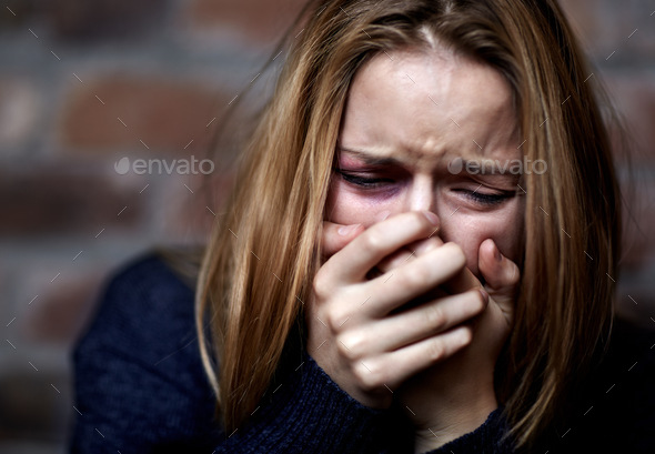 Emotionally victimized. Abused young woman crying hard and covering her ...