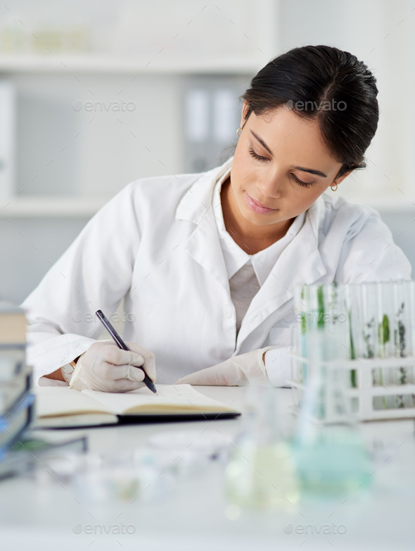 Working on a new theory of hers. Shot of a young scientist writing notes while working in a lab. - Stock Photo - Images