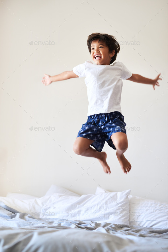 Flying solo. Full length shot of an adorable little boy playing and jumping on a bed at home.