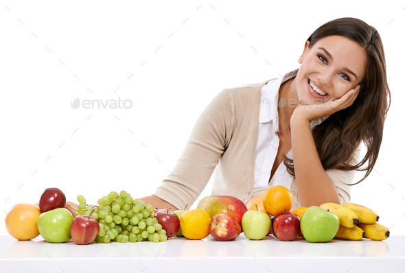 Enjoy natures bounty. A smiling young woman sitting beside a selection of fruits.