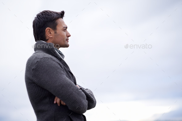 The weather is going to turn...Shot of a handsome man standing against a cloudy sky. - Stock Photo - Images