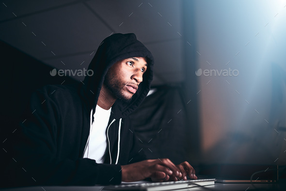 No code is uncrackable. Low angle shot of a young male hacker cracking a computer code in the dark.