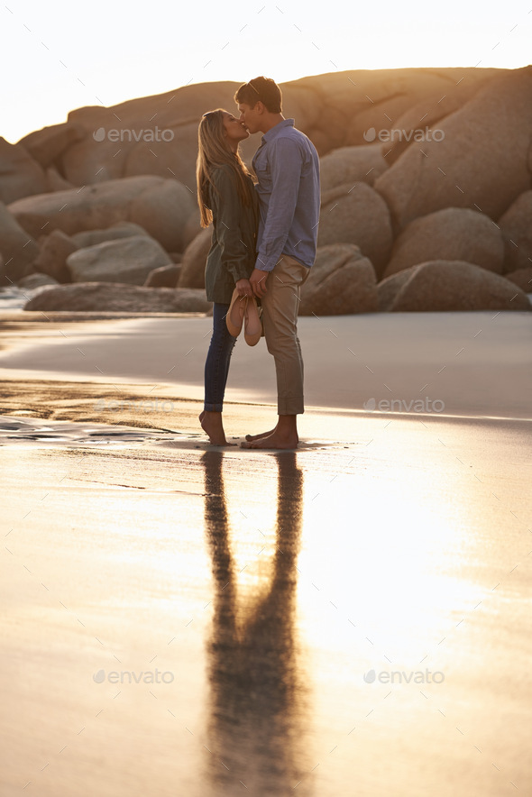 Lip locked. Shot of a young couple enjoying a romantic kiss on the beach at sunset.