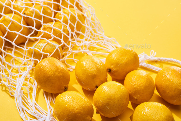 fresh ripe whole lemons in eco string bag on yellow background