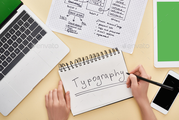 cropped view of designer writing typography lettering in notebook near website design template and
