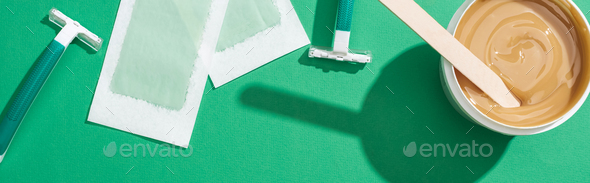 top view of green disposable razors, wax and depilation stripes on green background, panoramic shot