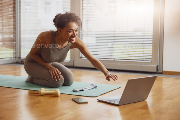 Afro american sporty woman sit on floor and preparing for online fitness class from home - Stock Photo - Images