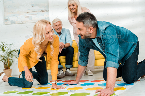 KYIV, UKRAINE - NOVEMBER 21, 2019: cheerful man and woman playing twister game near senior parents