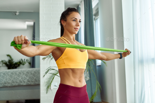 Young muscular build woman exercising with resistance band at home.