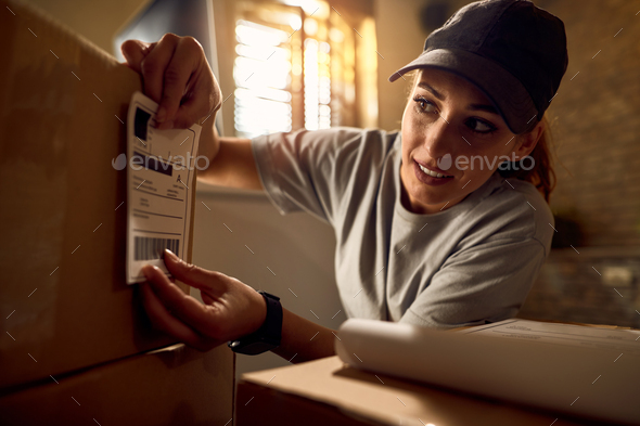 Female courier attaching address label on a package while working in the office.