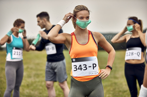 Athletic woman putting on face mask while participating in marathon race.