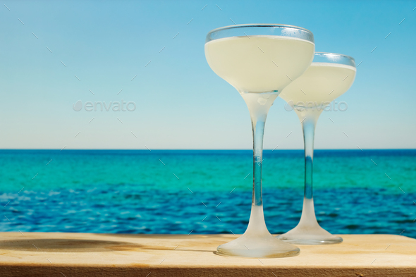 Two gimlet cocktails on table bar, sea on background.