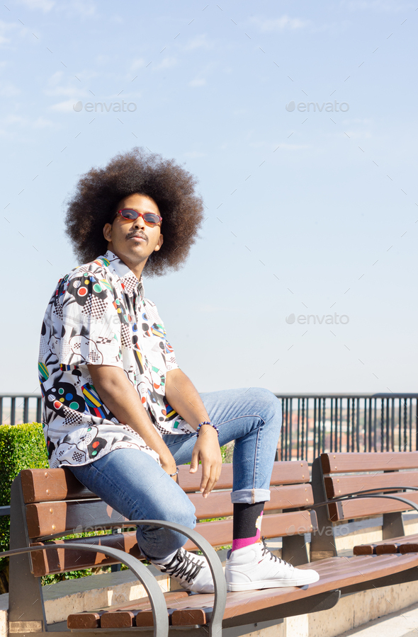 black guy with afro hair and red sunglasses sitting on the back of a bench