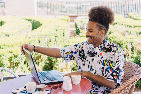 horizontal image of black guy with afro hair pulled back smiling working with a laptop