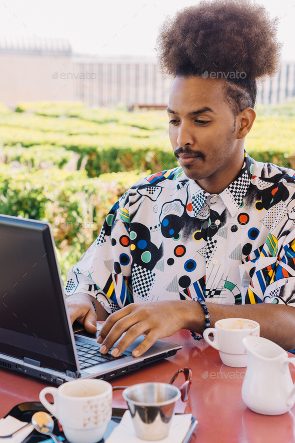 vertical picture of black guy with afro hair pulled back working with a laptop