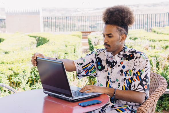 horizontal image of black guy with afro hair tied up with laptop