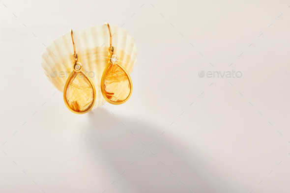 Gold earrings with rutilite stone hang on a sea shell on a light background