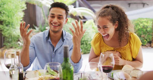 Diverse couple laughing with friends at dinner party on patio alt