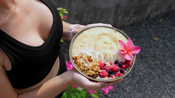 Hands Holding Banana Fruit Smoothie Bowl Served with Berries and Granola alt