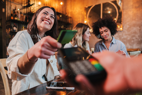 Happy young woman paying bill with a contactless credit card in a restaurant. Female smiling holding - Stock Photo - Images