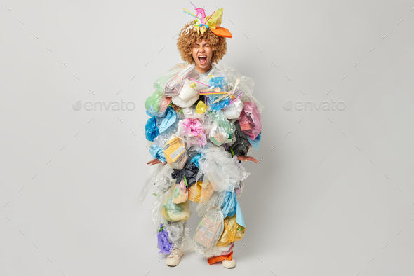 Studio shot of curly woman shouts loudly keeps mouth opened collects plastic rubbish tries to save
