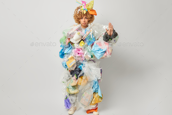 Photo of serious curly female volunteer makes stop gesture collects plastic garbage takes care of