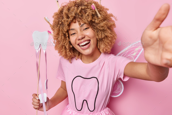 Horizontal shot of positive woman pretends being tooth fairy smiles broadly holds wand tells how to