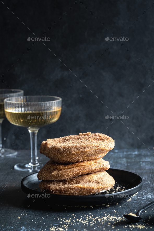 A stack of three apple beignets (apple fritters) on black background with glass of champagne