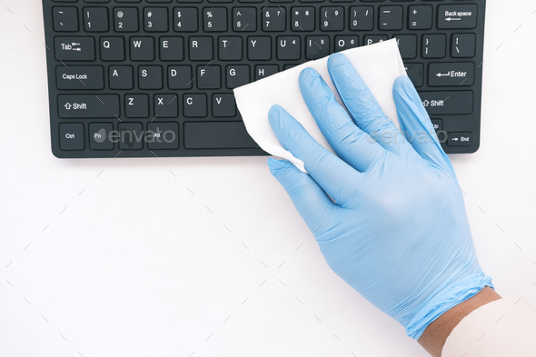 hand in blue rubber gloves and white tissue disinfecting keyboard