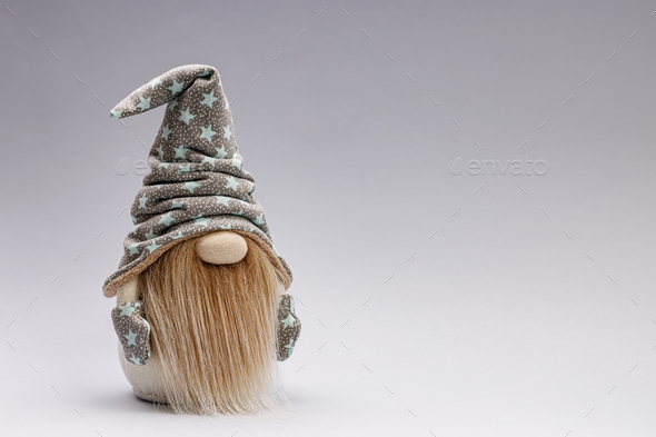 Cute bearded gnome in a cap with stars on a light background. Handmade soft toy. Copy space