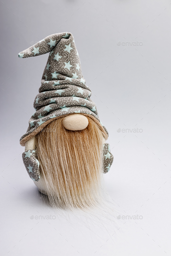 Cute bearded gnome in a cap with stars on a light background. Handmade soft toy. Copy space