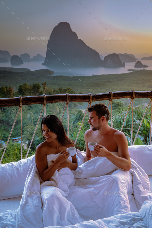 couple waking up in bed looking out over ocean during sunrise at wooden hut moutains of Thailand