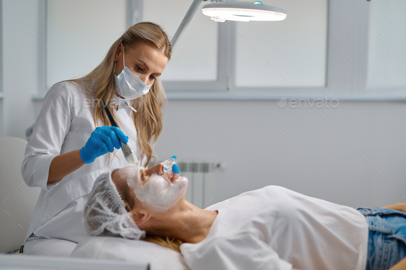 Beautician applying clay face mask on woman face side view