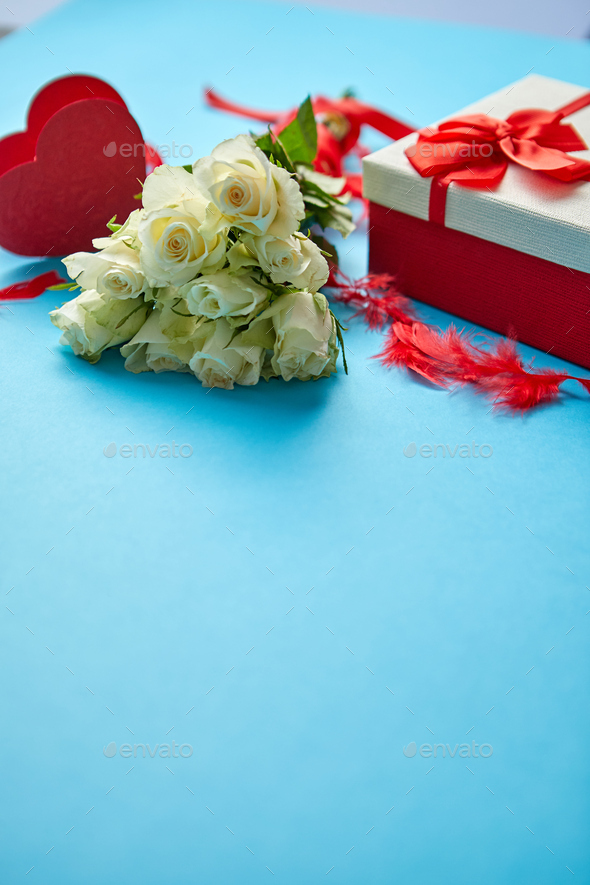Bouquet of white roses with red bow on blue background. Boxed gift on side - Stock Photo - Images
