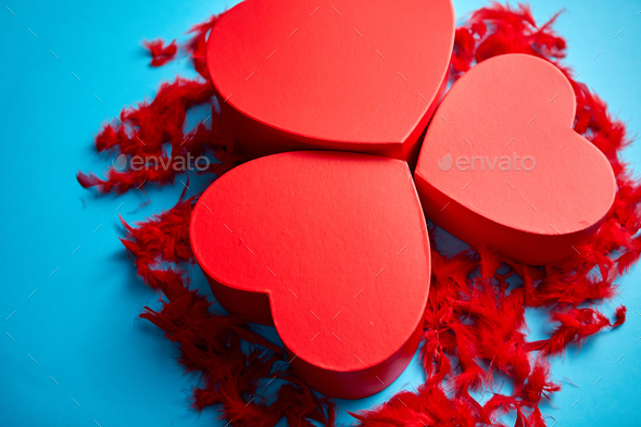 Three red, heart shaped gift boxes placed on blue background among red feathers - Stock Photo - Images