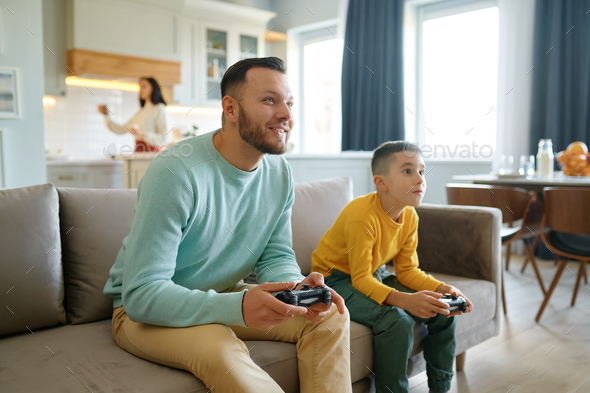 Dad and son playing video game while mom cooking on kitchen - Stock Photo - Images