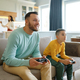 Dad and son playing video game while mom cooking on kitchen - PhotoDune Item for Sale