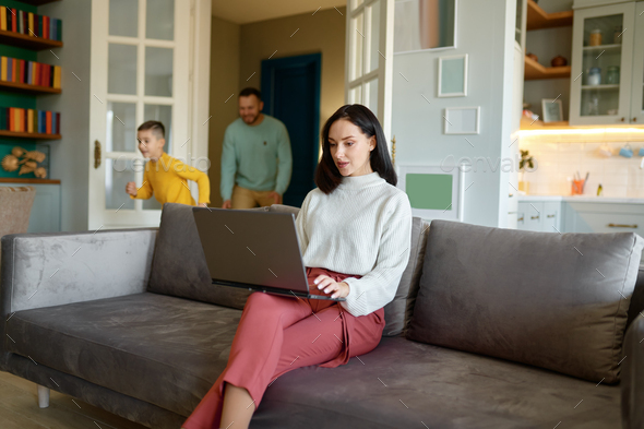 Young mother trying to work on laptop online while father and son playing - Stock Photo - Images