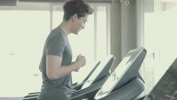 Handsome asian young man exercise with running on treadmill in the gym. alt