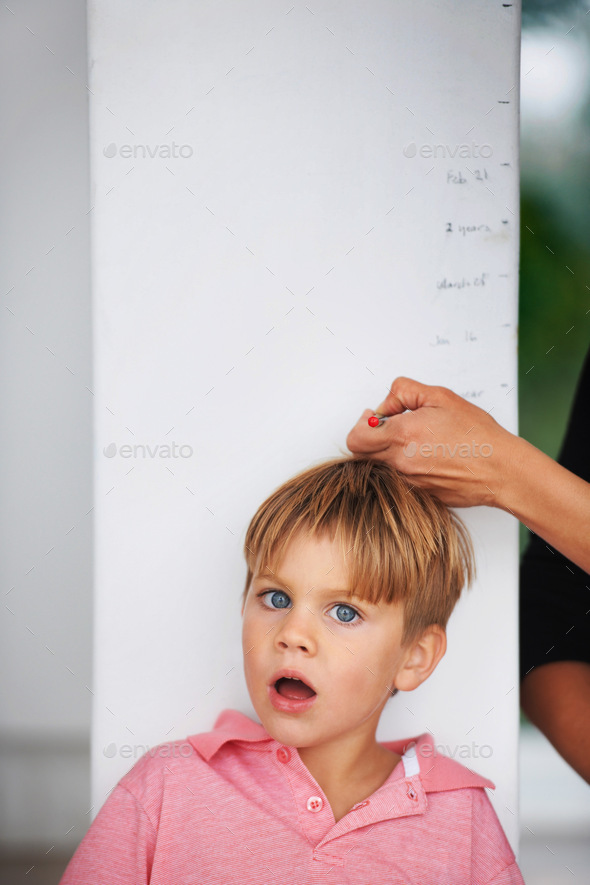 Portrait of a shocked young boy having his height measured by his mother on the kitchen wall