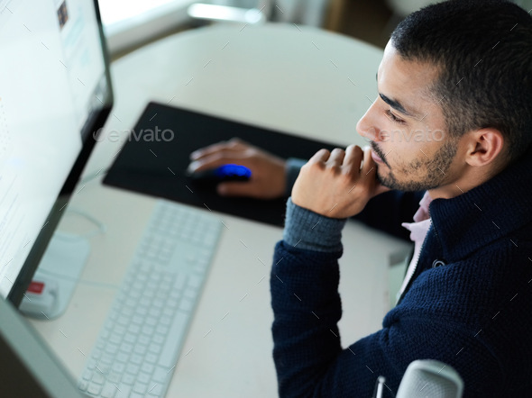 Shot of a focused young man sitting at a desk working on a computer with dual monitors