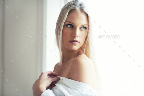 An attractive young woman standing in her bedroom with her shirt hanging off her shoulders