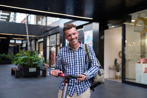 Smiling caucasian boy rides his electric scooter. Casual dressed man with his backpack