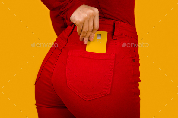 Unrecognizable woman putting yellow credit card in red pants