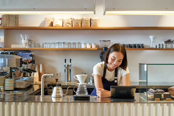 Happy smiling asian barista, girl behind counter, working with POS terminal  and brewing filter kit Stock Photo by benzoix