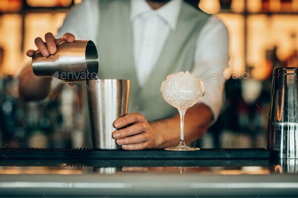 Barman pouring a cocktail into a silver shaker cup Stock Photo by wirestock